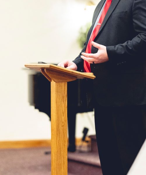Male wearing a black suit and preaching holding onto a pulpit